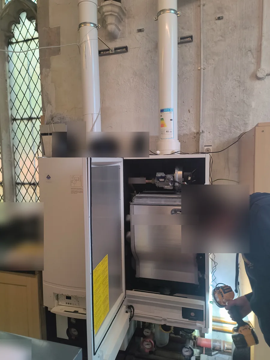 Engineer servicing a floor-standing commercial condensing boiler beside a leaded church window in Haverhill
